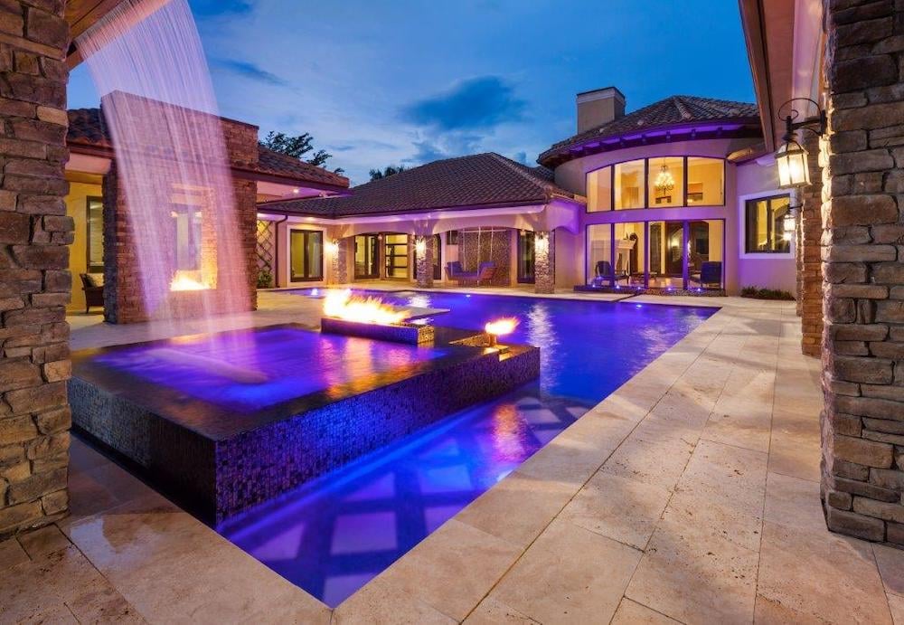 Backyard pool illuminated at night with colorful underwater lights